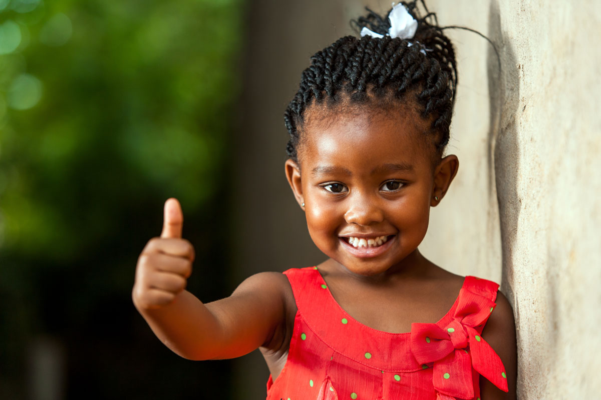 young girl smiles at the camera and gives a thumbs up