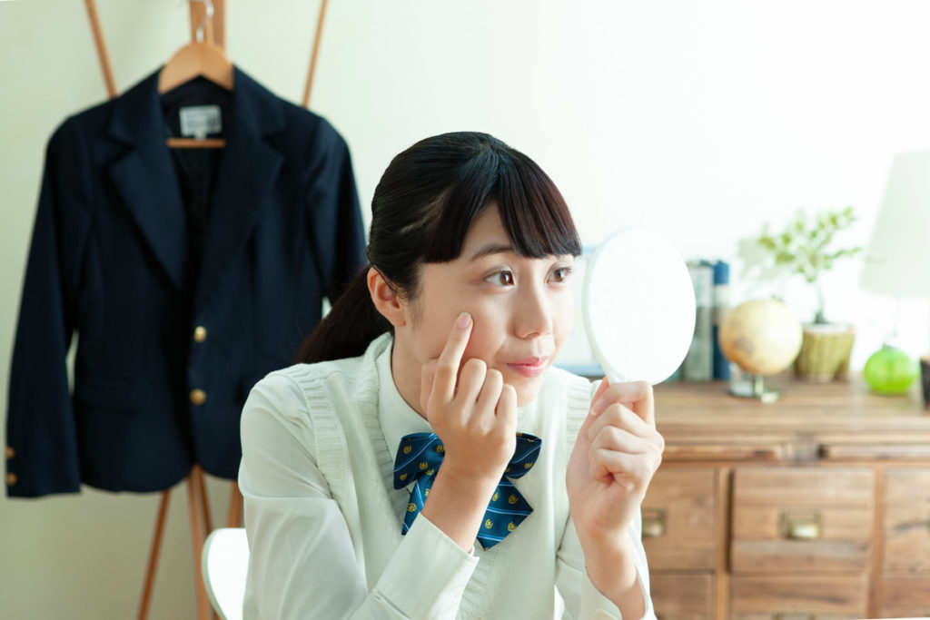 school girl checks her face for pimples in hand-held mirror