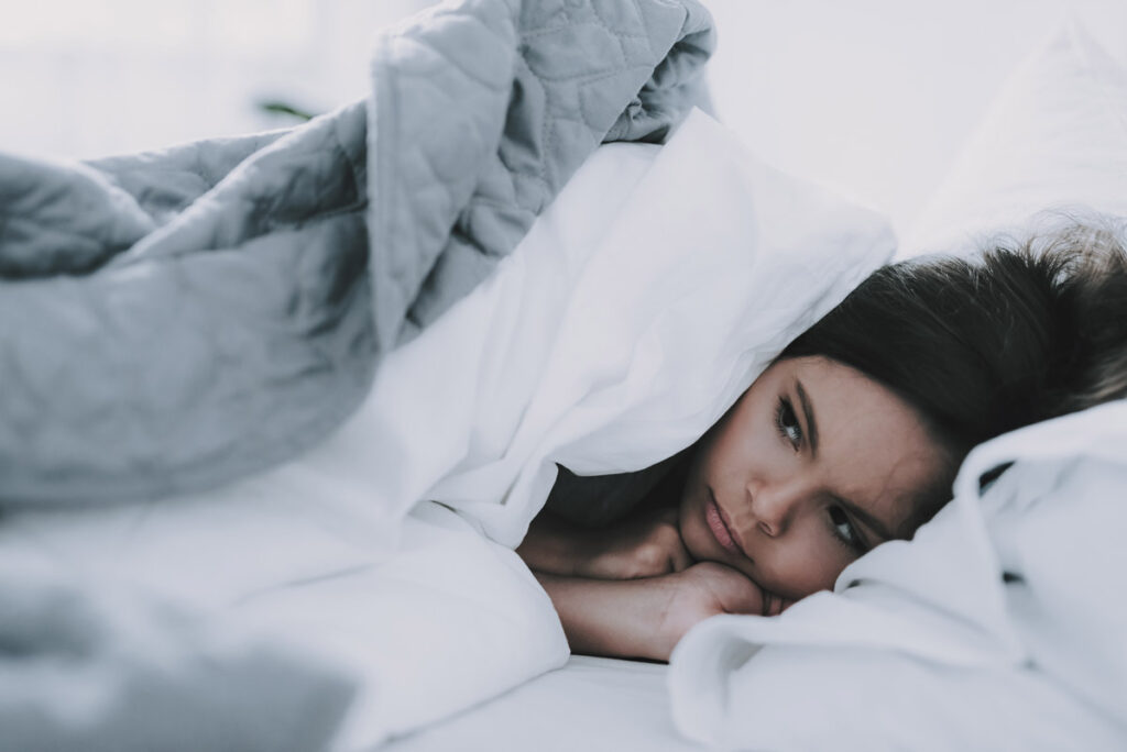 teenage girl lying in bed looking sad due to seasonal affective disorder